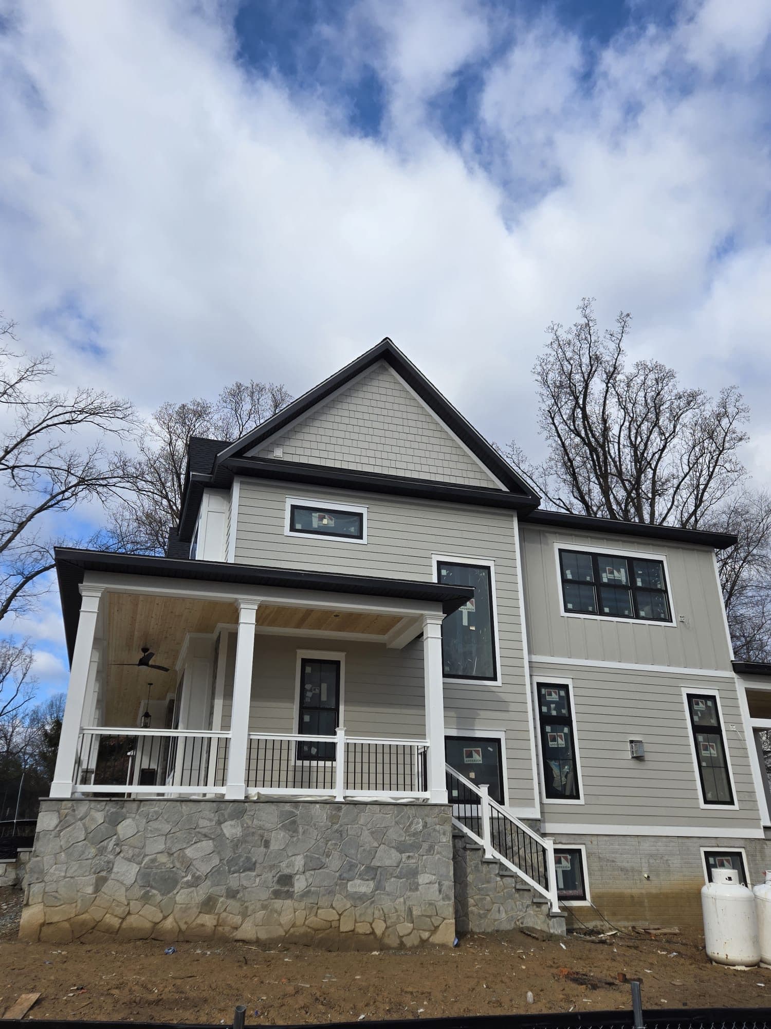 Home with light gray-beige shake and lap siding above a stone foundation and covered porch